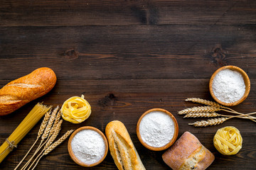 Bakery production, making bread and pasta. Fresh bread and raw pasta near flour in bowl and wheat ears on dark wooden background top view copy space