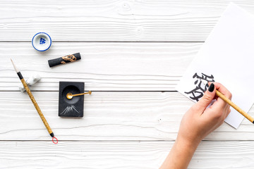 Calligraphy. Hand writes hieroglyph love on white paper on white wooden background top view copy space