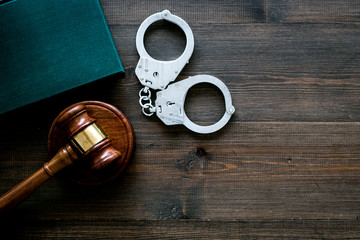 Crime concept. Metal handcuffs near judge gavel and law book on dark wooden background top view copy space