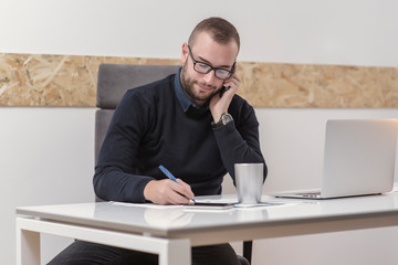 Naklejka premium young businessman working in his office and talking on his cell phone. business concept