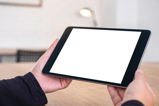 Mockup image of hands holding black tablet pc with blank white screen while sitting in office