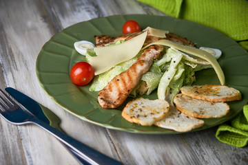 Fresh caesar salad in a green plate on a light wooden table