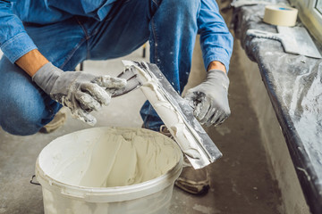 master is applying white putty on a wall and smearing by putty knife in a room of renovating house...