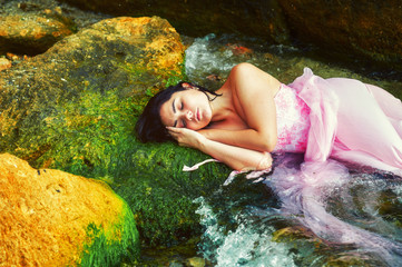 Young girl lying in the water in a pink dress .
