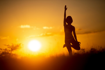 Fototapeta na wymiar woman standing in yoga pose with sunset background
