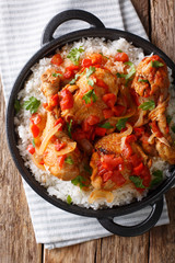 Haitian chicken in a spicy tomato sauce with rice side dish close-up in a pan. Vertical top view