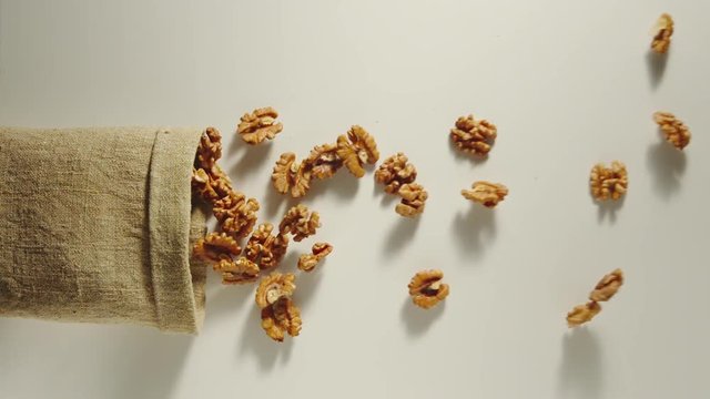 TOP VIEW: Bag falls and peeled walnuts are poured out of it on white background - Slow Motion