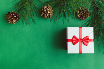 Christmas present gift box, golden pine cones and pine branches on the green color background with copy space.