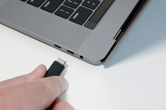 Man's Hand Plugging In Black USB Type C Cable Into USB-C Port On Laptop / Notebook Computer. Top Down View