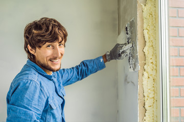 master is applying white putty on a wall and smearing by putty knife in a room of renovating house...