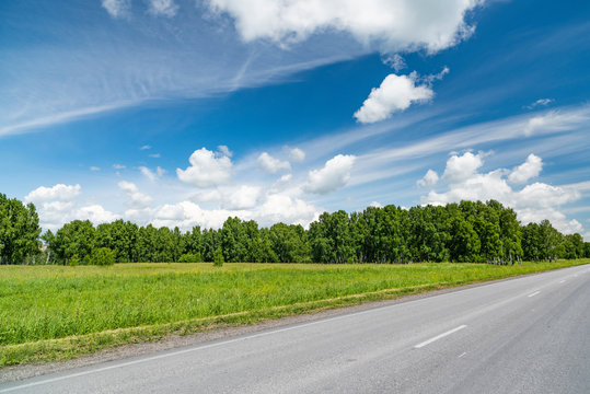 Summer landscape with asphalt road and blue sky with clouds.
