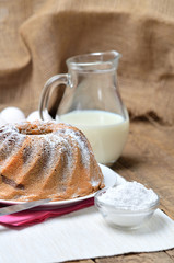 Homemade bundt cake sprinkled with sugar, milk and eggs in background
