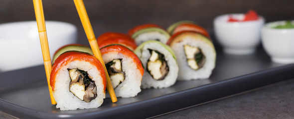 Sushi rolls on grey plate picked by bamboo chopsticks, wasabi, ginger, soy sauce on gray concrete table, dark background. Culinary, menuconcept. Close-up, copy space, layout design, horizontal format