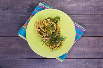 Zucchini pasta with peas in a plate on a wooden background. Vegan food