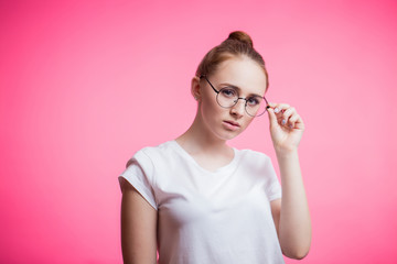 Close up portrait of beautiful woman wearing her red hair in bun, glasses and a white shirt on pink
