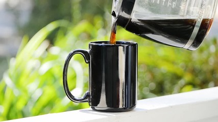 Atlanta, GA - November 15, 2018: Slow motion tight shot of pouring hot coffee slowly into a black mug on a white porch on a warm sunny day in Atlanta.