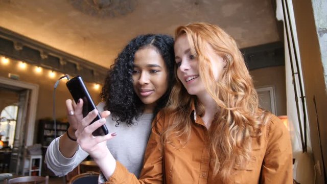 Multi Ethnic Girls Having Fun Using Smart Phone Technology In Cafe