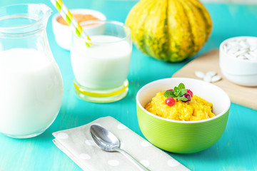 Pumpkin porridge with cranberry and mint in a white green plate on the table, ready to eat with milk