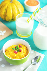 Pumpkin porridge with cranberry and mint in a white green plate on the table, ready to eat with milk