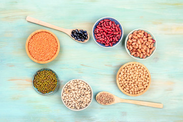 Various types of legumes, shot from the top on a teal background, forming a frame with copy space. Red kidney beans, lentils, chickpeas, soybeans, black-eyed peas