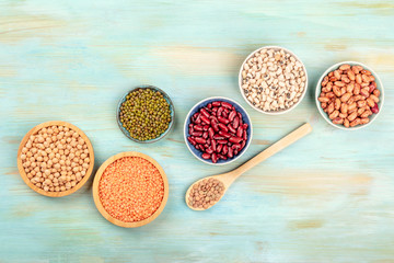Various types of legumes, shot from the top on a teal background with copy space. Red kidney beans, lentils, chickpeas, soybeans, black-eyed peas