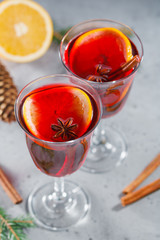 Two glasses with winter Christmas traditional mulled wine with orange slices, anise and cinnamon sticks among winter decorations.