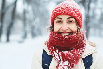 closeup portrait of a smiling woman in warm clothes, red knitted cap, scarf and mittens walking on...