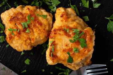 Two pieces of cordon bleu on a dark slate with a chopped green parsley