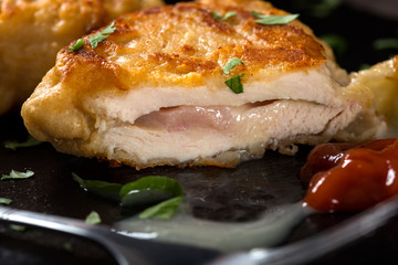 Piece of cordon bleu on a dark slate with a chopped green parsley