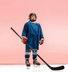 A hockey player in uniform with equipment over pink studio background. The athlete, child, sport,...