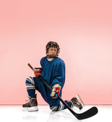 A hockey player in uniform with equipment over pink studio background. The athlete, child, sport,...