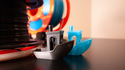 Two 3D printed boats on a black surface with 3D printer filament in the background.