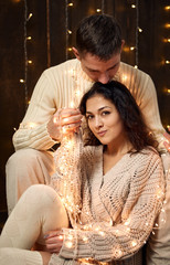 young couple is in christmas decoration and lights, fir tree on dark wooden background, new year holiday concept