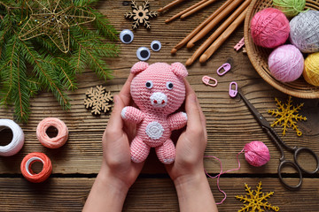 Pink pig, symbol of 2019. Happy New Year. Crochet toy for child. On table threads, needles, hook,...