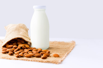 Almond milk in glass bottle with almond in sackcloth on the white table with gray background. with copy space for text.