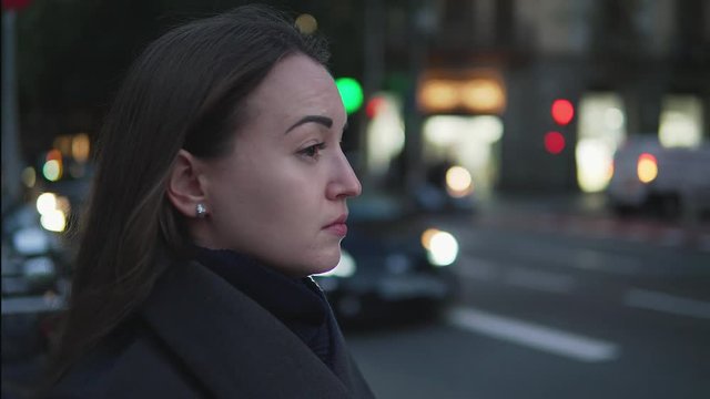 4k shot of a tired sad girl waiting to cross the street. City traffic on background.