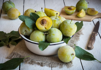 Fresh green plums in a bowl on white wooden table