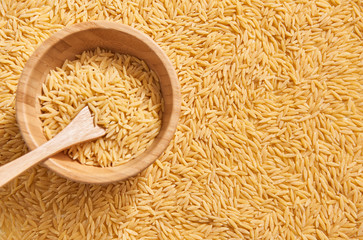 Wooden spoon in the wooden plate and many raw barley noodle.