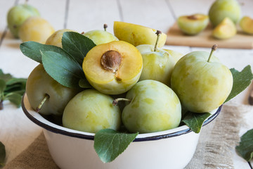 Fresh green plums in a bowl on white wooden table