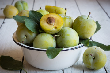 Fresh green plums in a bowl on white wooden table