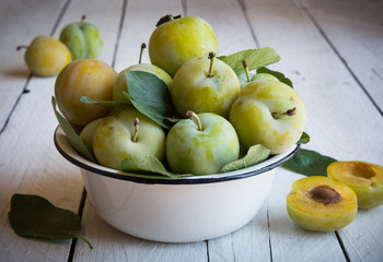 Fresh green plums in a bowl on white wooden table