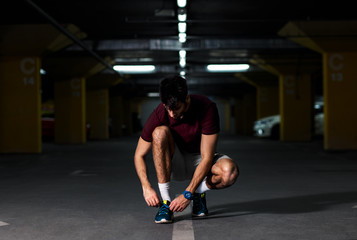 Fototapeta na wymiar Portrait of young male athlete tying shoelaces and preparing to run in the underground car parking.