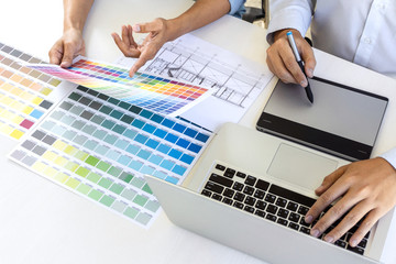 Team of colleague graphic designer drawing and retouching image on graphics tablet and choose color swatch samples for selection on laptop computer