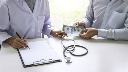 Patient giving bribe money the form of dollar bills to Female doctor while give success the deal to contract agreement, Bribery and corruption concept