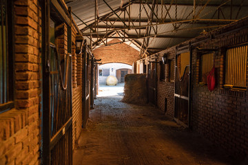 Inside a bricks stable looking trough a door  two hay rolls and horses stals - obrazy, fototapety, plakaty