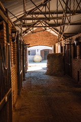 Inside a bricks stable looking trough a door  two hay rolls and horses stals