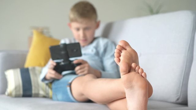Feet close up footage of teenager's boy lying on the cozy sofa and  enthusiastically plays game using the gamepad with smartphone. Health vision concept 4K UHDTV