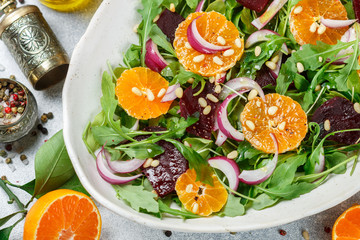 gourmet salad of arugula, baked beetroot, tangerines and red onions with spices and pine nuts in a...