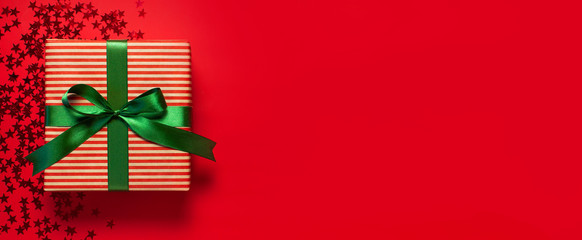 Gift box with green ribbon and holographic glitter confetti form of stars on red background top view flat lay. Holiday concept, birthday gift, new year or Christmas gift box presents Xmas holiday