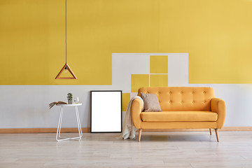 Yellow wall background, yellow sofa and wooden lamp. Empty frame decoration.